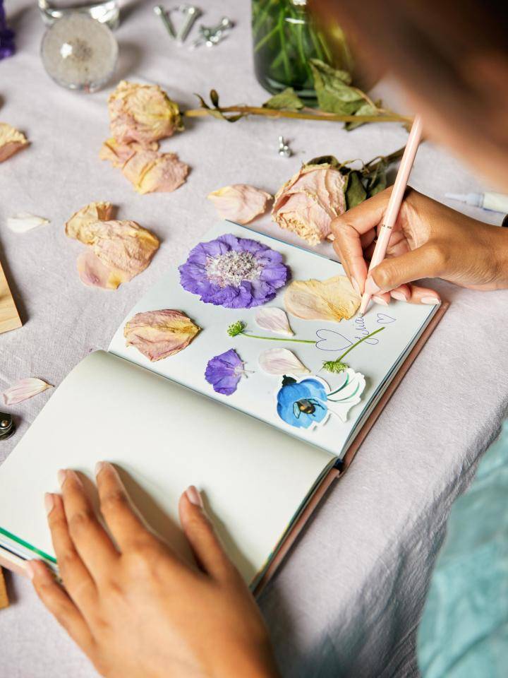 Hand plaatst gedroogde bloemen in een poëziealbum op een houten tafel.