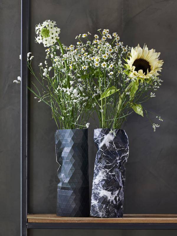 Twee vazen met kamillebloemen en een zonnebloem op een houten plank tegen een grijze achtergrond.