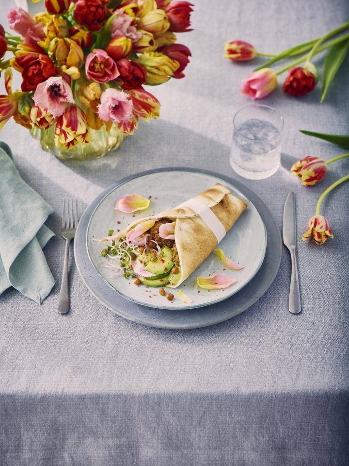 Humus falafel wrap on a plate with tulips in a vase and scattered on a table.