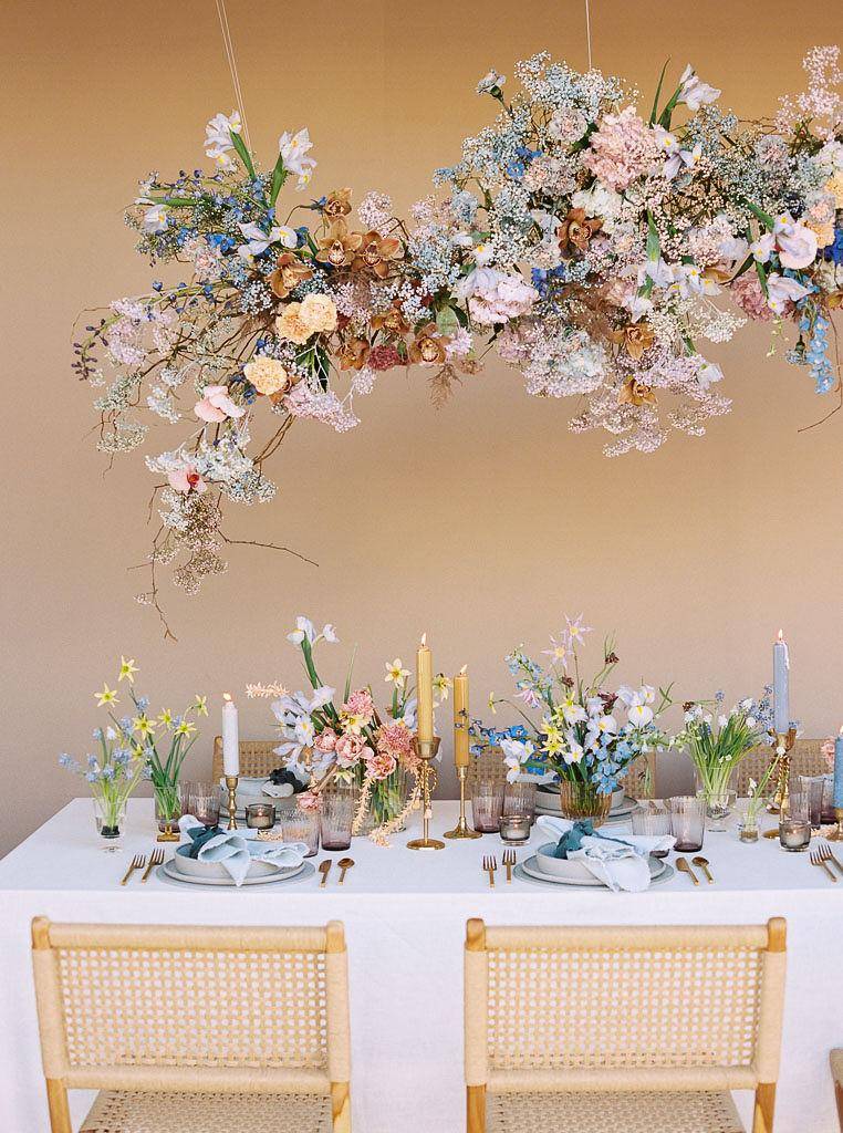 Eettafel met bloemstukken, kaarsen en gedekte borden, met een dromerige bloemenwolk erboven.