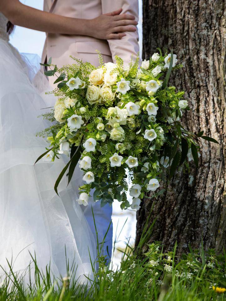 Koppel bij een boom, met een boeket van witte en lichtgele bloemen en groene bladeren.