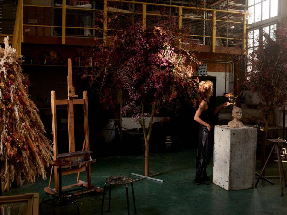 Kunstenaar werkt aan een sculptuur in een atelier met droogbloemen en schildersezel.
